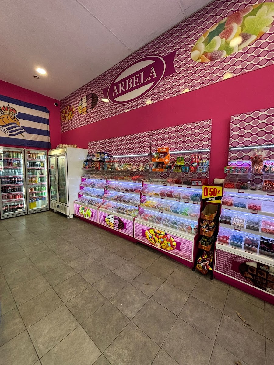 Interior de Arbela: paredes rosas, cubetas de golosinas a granel y neveras con refrescos